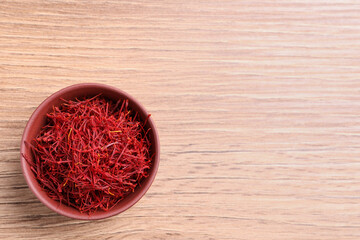 Fototapeta na wymiar Dried saffron in bowl on wooden table, top view. Space for text