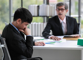 Asian businessman office workers sitting with serious emotions because he was blamed by a senior leader for errors of a working project. Selective focus at the young man with blurred elderly manager