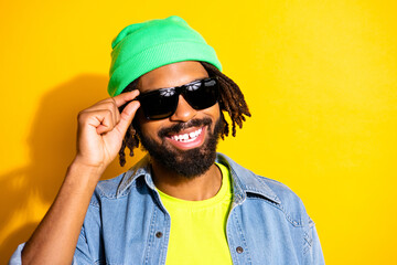 Photo of young handsome positive smiling in sunglasses wear green beanie look copyspace isolated on yellow color background
