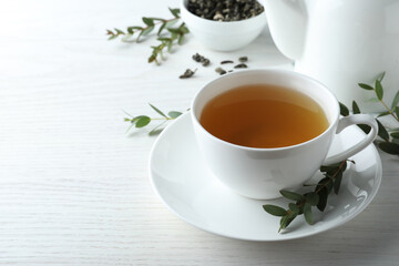 Cup of green tea and eucalyptus leaves on white wooden table. Space for text