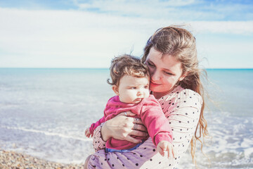 Happy family moment of a young mom enjoying a day on the beach with her baby