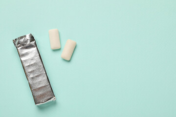 Pack and chewing gum pieces on turquoise background, flat lay. Space for text
