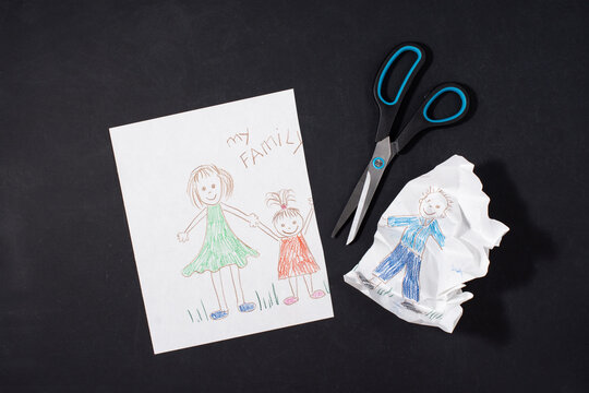 Child's drawing of a family on paper. Mom, dad and baby are holding hands. Family divorce concept. The father's image is cut with scissors. Relationship problems and difficulties