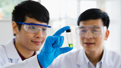 2 Scientist asian adults man wearing eyeglass look at glassware as green liquid in laboratory