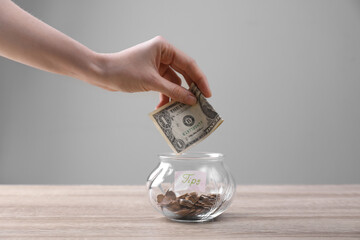 Woman putting tips into glass vase on wooden table, closeup