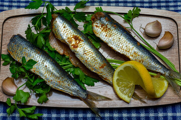 Top view of fresh Mediterranean sardines on the wooden carving board with lemon and garlic and herb