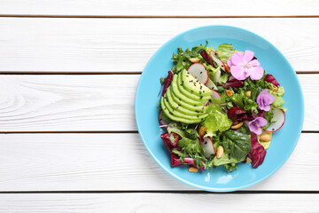 Fresh spring salad with flowers in plate on white wooden table, top view