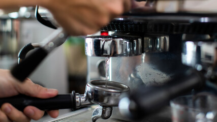 Close up of warm water rinsing at the pouring from coffee machine. A man barista preparing for pressing ground coffee for brewing espresso or americano in a cafe.
