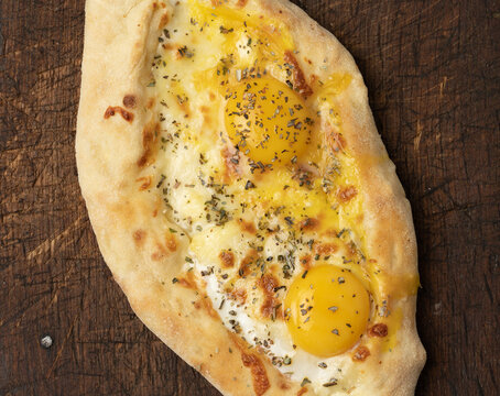 baked adjarian khachapuri with whole egg yolk on wooden board