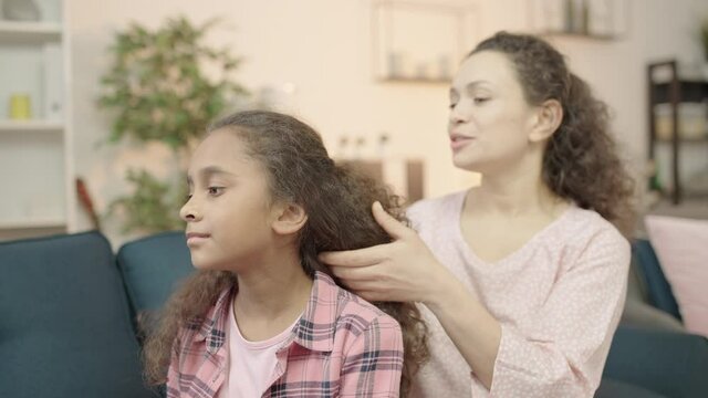 Mother carefully combing daughters hair, morning routine, family traditions