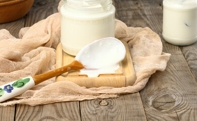 homemade yogurt in a glass transparent jar on a wooden table, a healthy fermented milk product