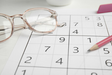 Sudoku, pencil and eyeglasses on white table, closeup