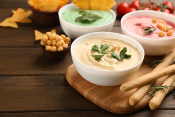 Different kinds of tasty hummus served with bread sticks on wooden table