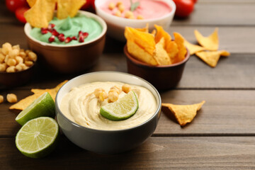Different kinds of tasty hummus with ingredients on wooden table