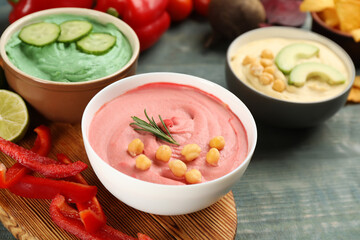 Different kinds of tasty hummus with ingredients on light blue wooden table