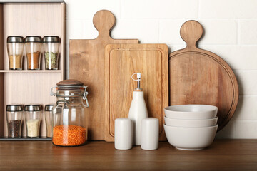Fototapeta na wymiar Set of spices and different dishware on wooden table near white brick wall in kitchen