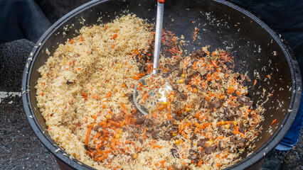 Texture of the finished pilaf in the cauldron. Tasty pilaf is cooked on the street in a large...