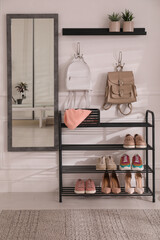 Black shelving unit with shoes and different accessories near white wall in hall. Storage idea