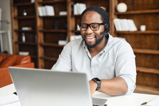 A multiracial guy using a hands free device for online communication sitting at the desk in modern office space, an African-American wearing headset holding video conference, webinar - Powered by Adobe