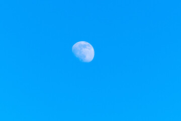 moon is in the blue sky during the day, three days before the full moon.