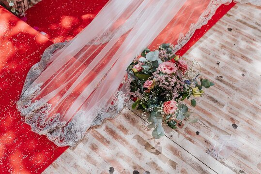 Velo de novia mientras camina sobre alfombra roja. Detalle floral en una boda. Arreglo de flores. Decoraci&oacute;n floral de evento. Velo.