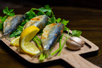 Close up of fresh Mediterranean sardines on the wooden carving board with herbs and lemon and garlic, nutrition concept 