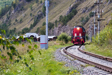 Red vintage train running by railway at the foot of a mountain. Summer travel concept.