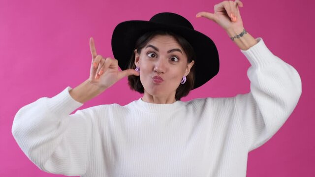 Woman in casual white sweater and hat on pink background isolated funny crazy does grimaces fool day     