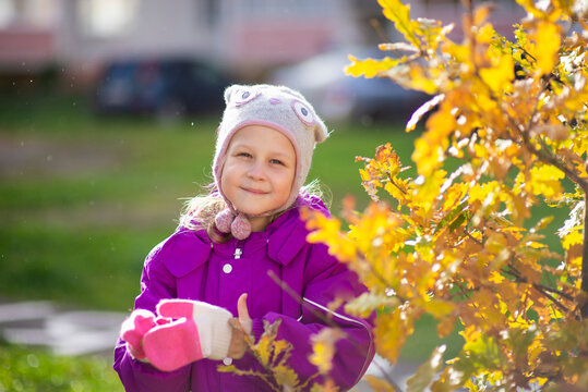 A small child in an autumn suit and a funny hat on the lawn under the open sky is cute stomping and smiling. It's autumn outside, yellow leaves on the trees, a clear sunny day. image with selective