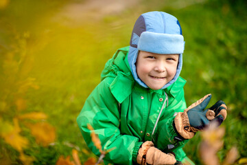 A small child in an autumn suit and a funny hat on the lawn under the open sky is cute stomping and smiling. It's autumn outside, yellow leaves on the trees, a clear sunny day. image with selective