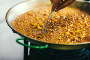 Cooking paella chef checks readiness with tweezers - Spanish food