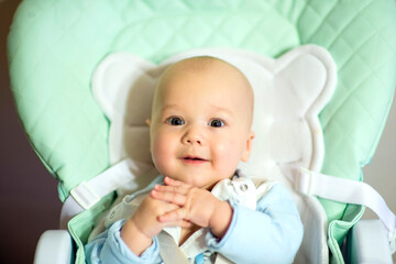 A funny little boy is sitting in a feeding chair.Family morning at home. . image with selective focus