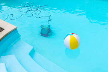 Fototapeta na wymiar Underwater Robot cleaning a swimming pool and a inflatable ball floating. Copy space