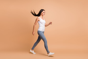 Fototapeta na wymiar Full length side profile photo portrait of walking woman isolated on pastel beige colored background
