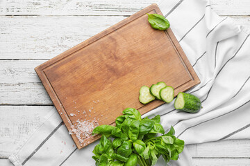 Cutting board with cucumber and basil on light wooden background