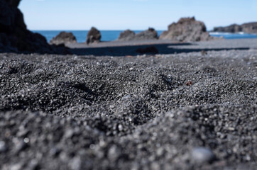 Black sandy beach in Iceland. Focus on the stones and grains in the foreground, blurred background....
