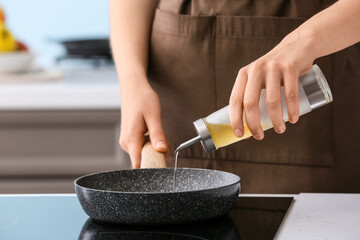 Woman pouring oil onto frying pan in kitchen