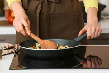 Woman cooking vegetables on electric stove in kitchen