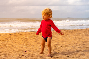 BLOND CHILD WITH RED T-SHIRT, ON THE BEACH, WITH SUN HITTING ON THE FACE.