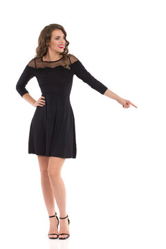 Elegant Young Woman In Black Cocktail Dress And High Heels Is Standing And Pointing Down