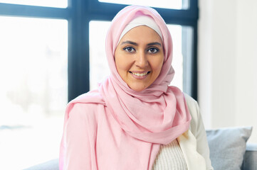 Portrait close-up of a charming young Muslim Arab businesswoman office manager in pink hijab smiling and facing the camera, standing in the office with panoramic view, ready to work and help clients