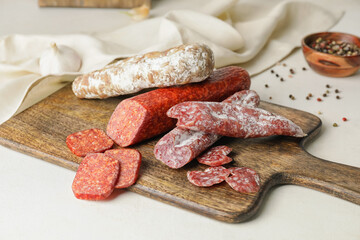 Cutting board with tasty sausages on light background