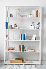 Fototapeta na wymiar Shelf unit with books and decor near light wall