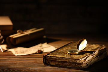 Old book with compass on table against dark background, closeup