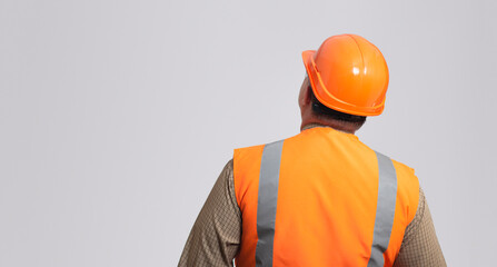 back of contruction worker in hard hat and reflective vest on grey studio background looking,...