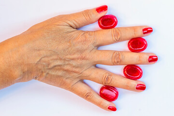 The back of a female hand rests on a white surface with red candies between one finger and the other