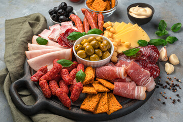 Meat snacks of different types, cheese and olives on a dark gray background.