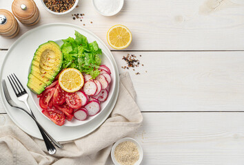 Fresh vegetable salad on a white wooden background. Pieces of avocado, radish, tomato and lettuce leaves seasoned with sesame seeds and spices.