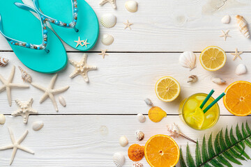 Colorful summer background. Cocktail with ice, oranges, lemons, shells, starfish and flip-flops on a light wooden background.