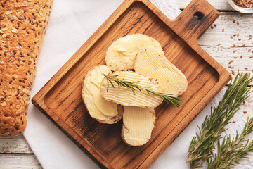 Slices of fresh bread with butter and rosemary on light wooden background